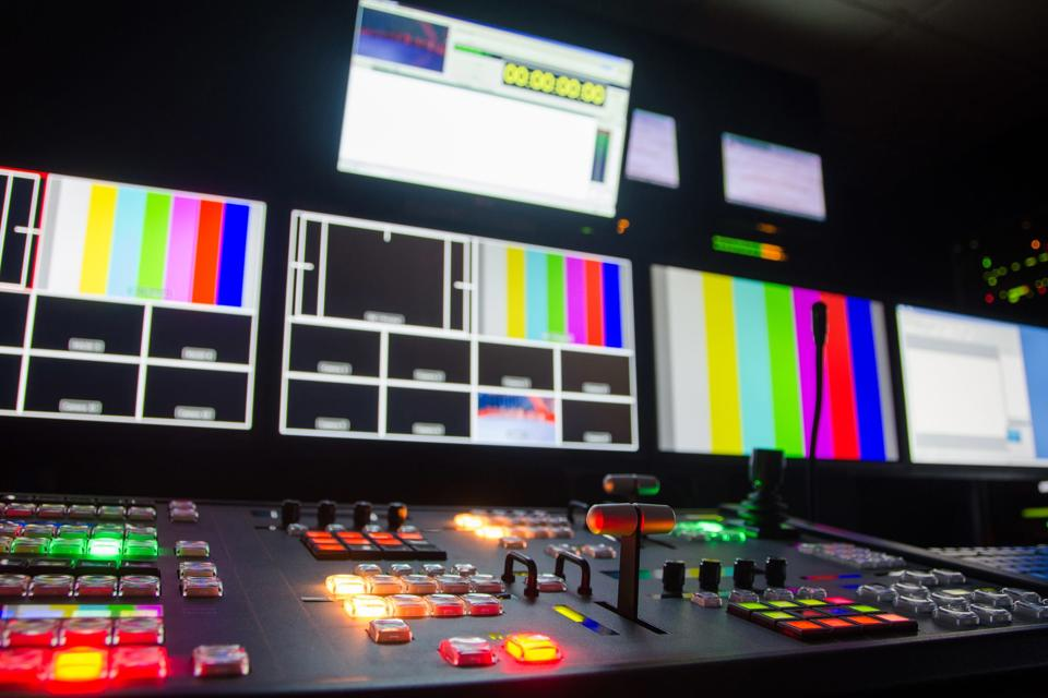 Inside a control room, with control panels and multiple screens 