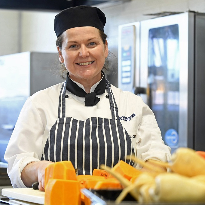 Melbourne polytechnic food staff member smiling at camera while they prepare food.