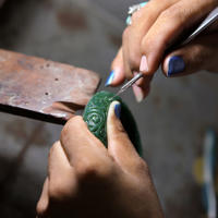 A person crafting patterns through the wax with a carving utensil