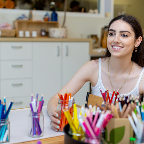 Claudia sitting in front of jars full of coloured pencils