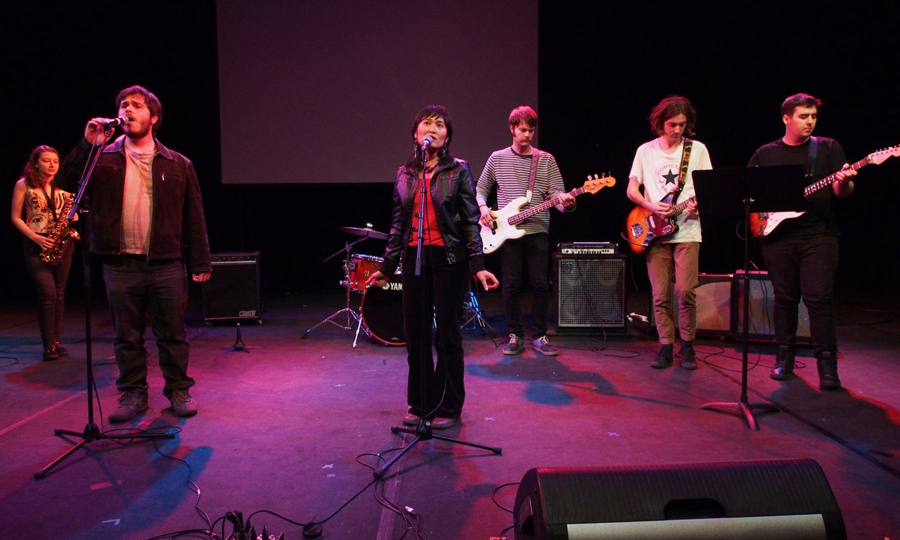 Music students singing on stage, with musicians playing saxophone and electric guitars