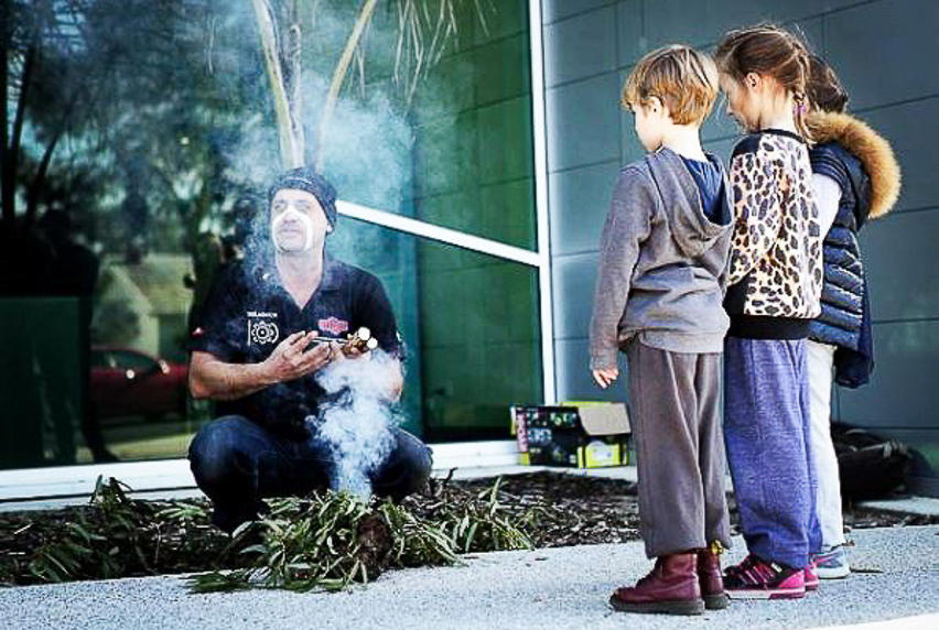 Man engaged in smoking ceremony while three children observe