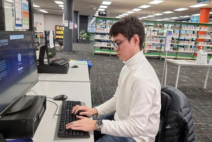Man wearing a white turtleneck crew while sitting at computer in a Melbourne Polytechnic Library 