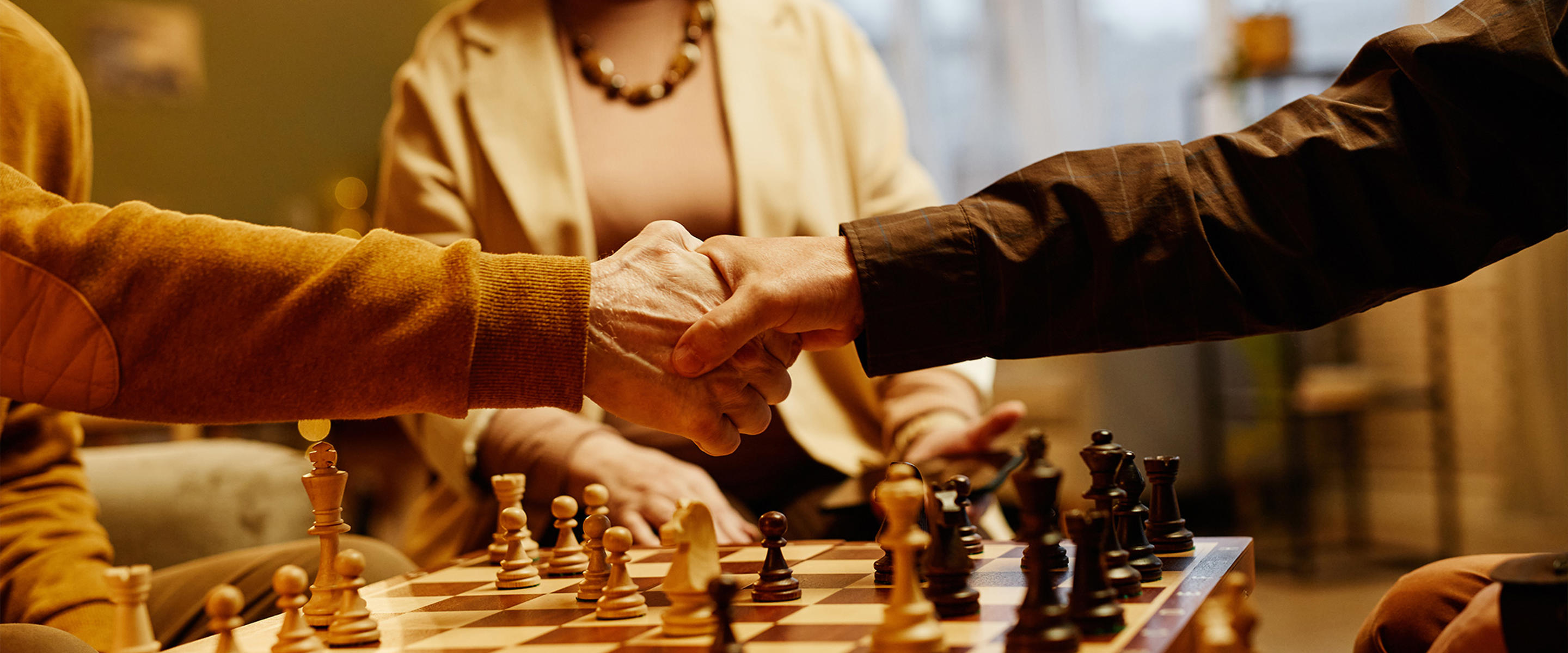 Cropped image of two people's arms in a handshake, reaching across a chessboard, in an aged care setting